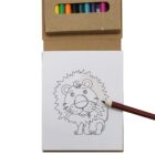 A coloring book page featuring a cartoon lion illustration is being colored. A hand holds a colored pencil to fill in the lions mane. A box of colored pencils is visible above the page.