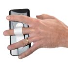 A hand holding a smartphone with a white grip attached to the back. The fingers slide through the grip for secure handling. The person is wearing a gold ring on the ring finger. The phone is black and rectangular.