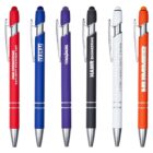 Six colorful ballpoint pens are lined up vertically. Each pen is a different color: red, blue, purple, black, white, and orange. They have silver clips and tips, and each features a printed brand name in white text.