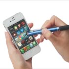 A person using a blue stylus on a white smartphone with various colorful app icons displayed on the screen.