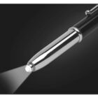 Close-up of a sleek metal pen with a built-in LED light on its tip, shining a beam on a dark background.