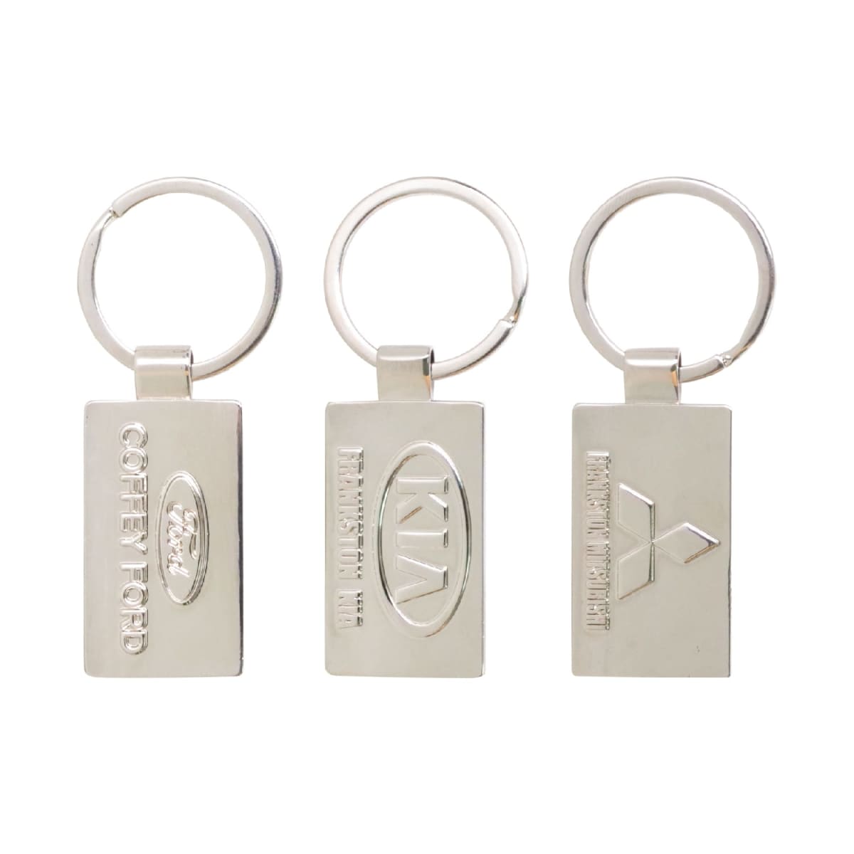 Three rectangular silver metal keychains with embossed logos. Each keychain has a different logo in the center, including Ford, Kia, and another logo, with accompanying text. The keychains have round metal rings for attaching keys.