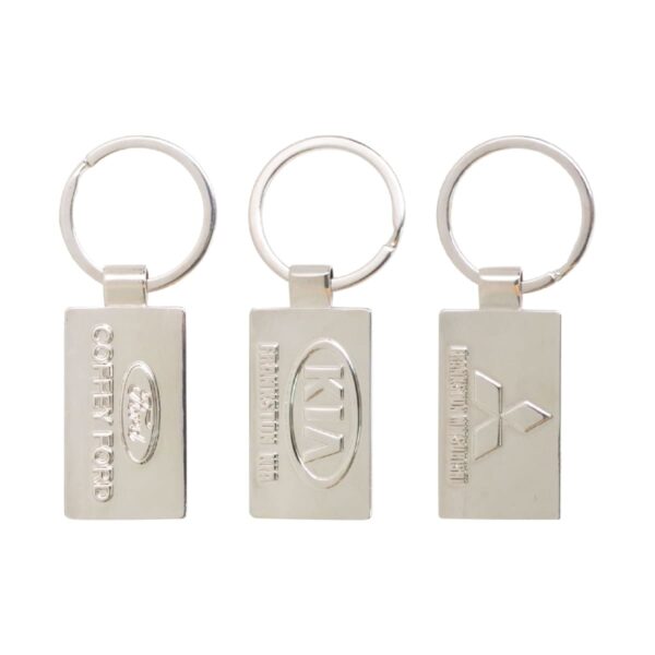 Three silver keychains feature embossed logos: one with Coffey Ford and a Ford logo, another with a Kia logo and Harrison Kia, and the third with Mitsubishi and Carson Mitsubishi. All are rectangular with a ring.