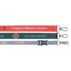 Three lanyards with clips: one red with I Support Bowel Cancer, one green with John Smiths Stadium and a logo, and one gray with Qube Logistics and a logo, featuring a plastic buckle.