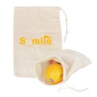 Two beige drawstring bags are shown. One is upright with Smile printed in yellow. The other bag lies open, containing a partially visible orange and an apple.