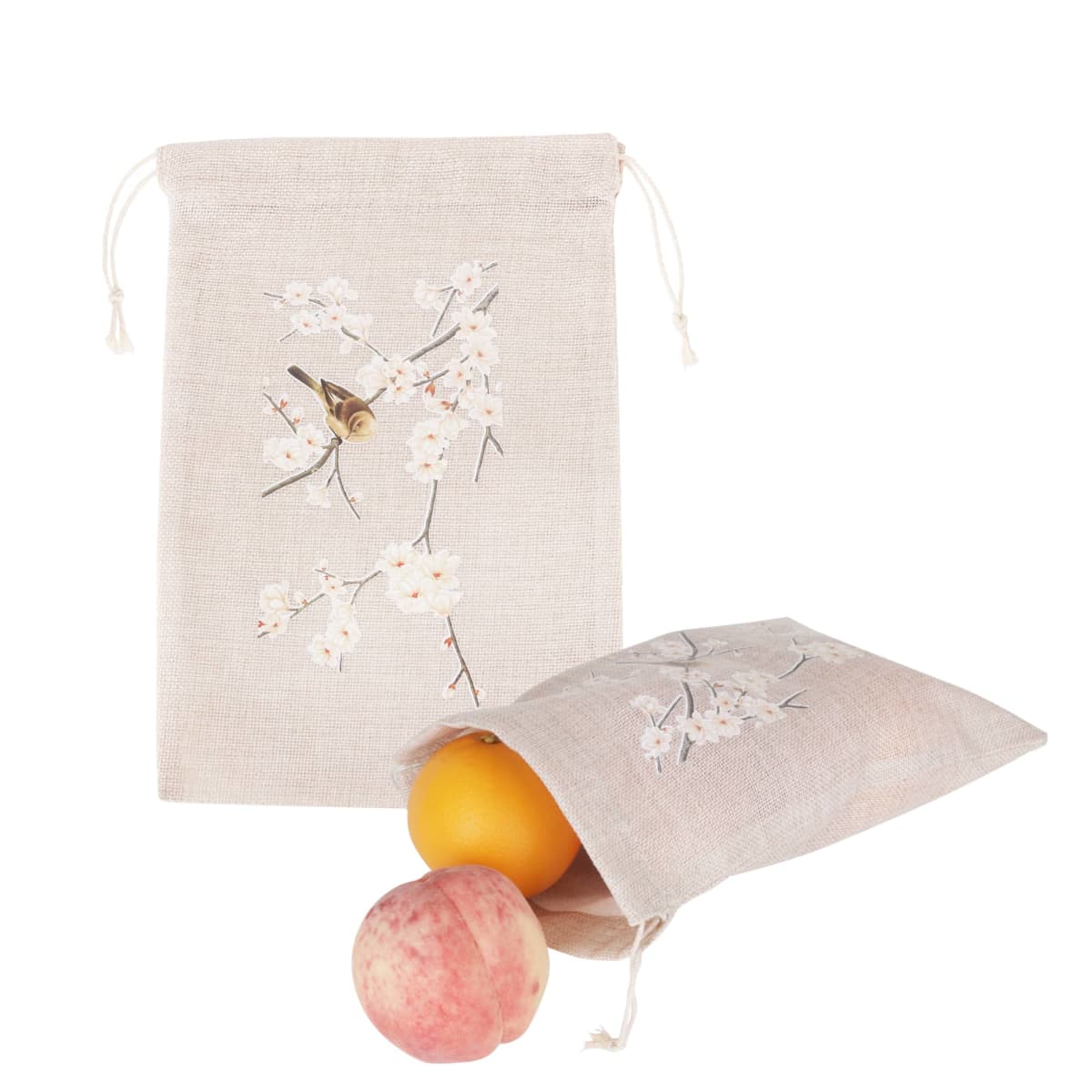 Two beige drawstring bags with floral designs. One bag is upright, displaying a branch with flowers. The other bag is tipped over, revealing a peach and an orange partly outside.