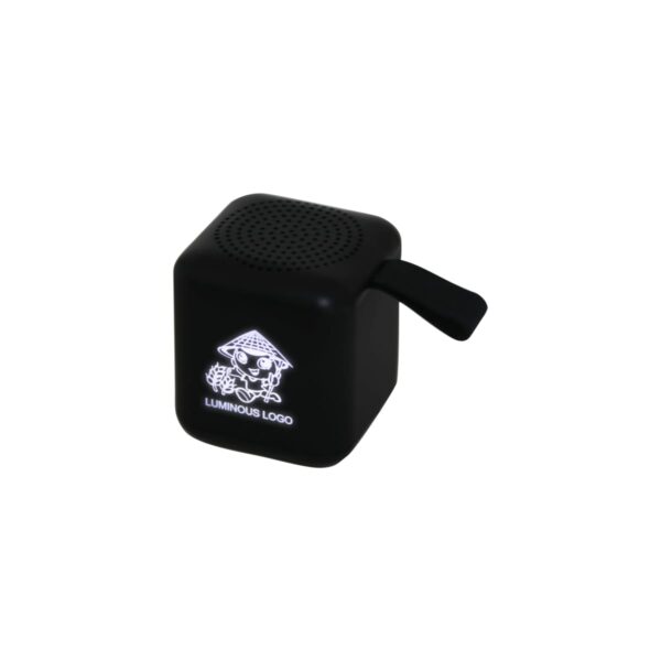 A black cube-shaped speaker with a small handle and a glowing luminous logo on one side, featuring a playful design with a hat and sunglasses.