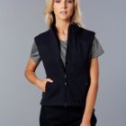 A person is wearing a black zip-up vest over a gray t-shirt and black pants. They have shoulder-length blonde hair and are standing against a plain gray background.