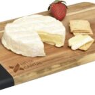 Wooden cheese board with a wheel of brie, two strawberry halves, and crackers. The board has a black handle edge and a Helix Capital logo.