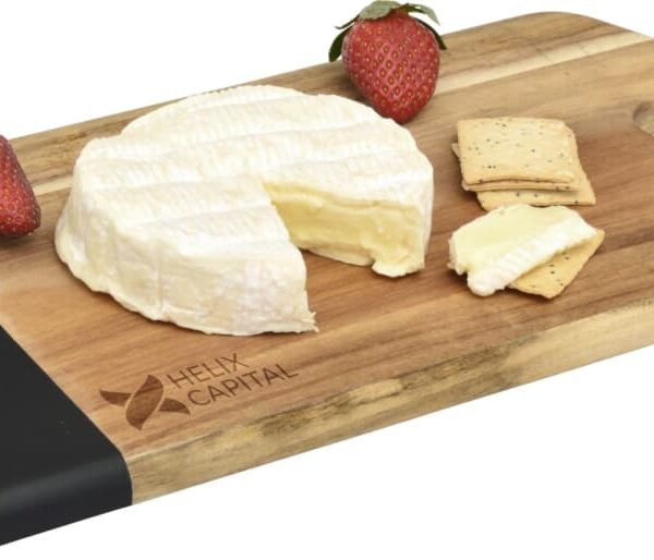 A wooden cutting board with a black handle features a round wheel of soft cheese with a wedge cut out, surrounded by two whole strawberries and two pieces of square cracker, one topped with a cheese slice.