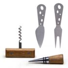 A set of wine and cheese tools, including a corkscrew with a wooden horizontal handle, two cheese knives with holes in their metal handles, and a bottle stopper with a metal top and wooden grip, all arranged on a white background.