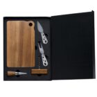 A black box contains a wooden cutting board, a cheese knife, a cheese fork, a wine stopper, and a corkscrew. The utensils have wooden handles.