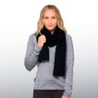 A person with blonde hair wearing a gray long-sleeve top and a black scarf stands against a light gray background. They are looking ahead, holding the scarf with one hand.
