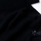 A close-up of a textured black fabric, displaying a soft, ribbed pattern. A small black label is visible, attached to the fabric on the right side, containing care instructions and brand details.