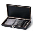 A set of six knives with black handles neatly arranged in a black wooden box with a hinged lid. The box is open, displaying the knives, which have shining blades and polished handles.