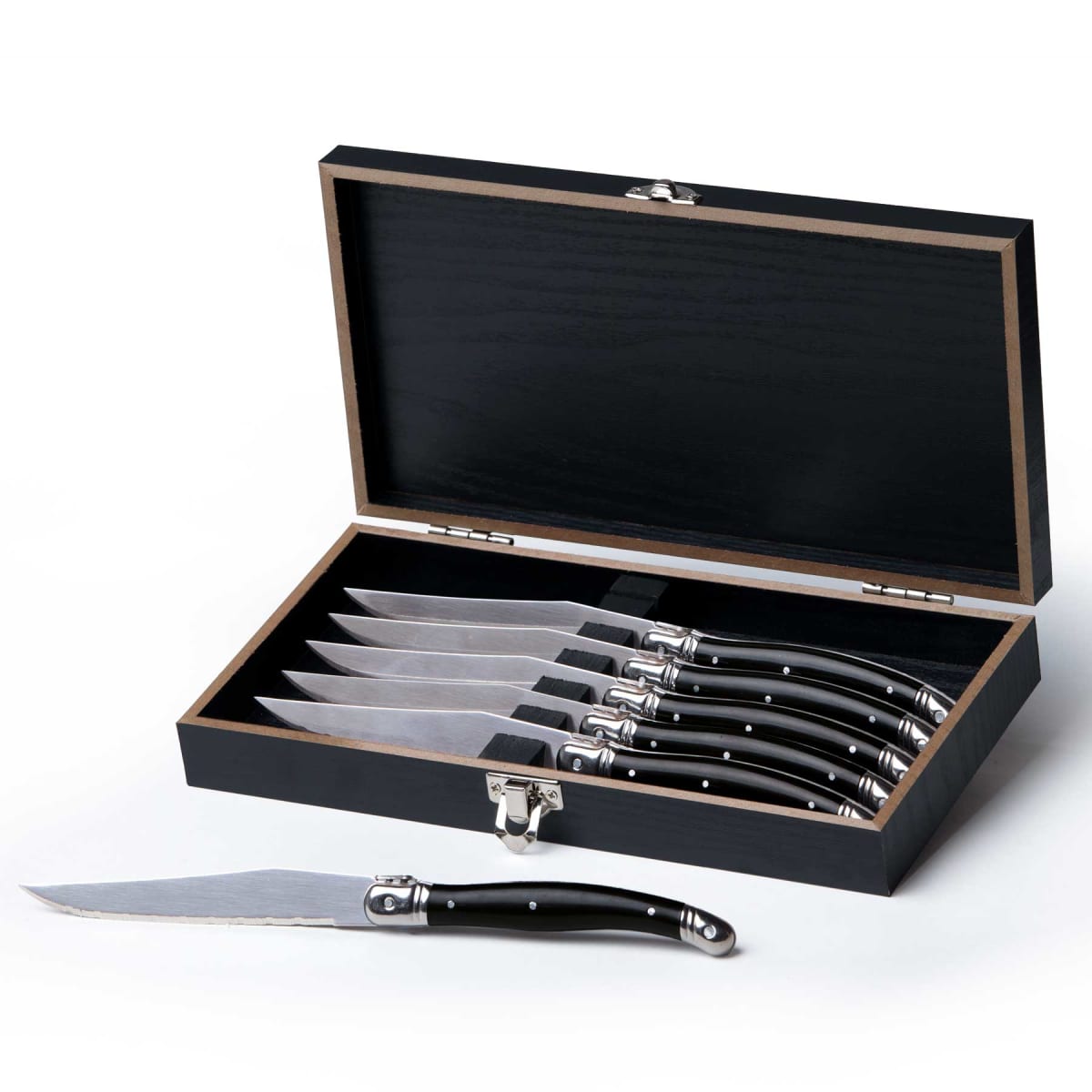 A set of six steak knives with black handles displayed in an open black box. One knife is placed in front of the box, showing its blade and handle. The box has a silver clasp for closure.