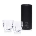 Two twisted design whiskey glasses next to a black cylindrical box. The box features a simple drawing of a glass and the words po di fame.