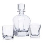 A clear glass decanter with a stopper is placed between two empty square-shaped glass tumblers. The set is arranged on a plain white background.
