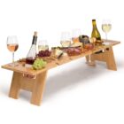 A wooden picnic table holds wine glasses, bottles, assorted cheeses, grapes, crackers, and nuts. The table is designed with slots to securely hold wine glasses and bottles.