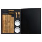 A black box set containing a wooden serving board, three cheese knives with wooden handles, two wooden spoons, and two white ceramic bowls, arranged neatly in designated compartments.