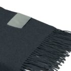 A close-up of a dark-colored fabric with fringed edges. A small rectangular label is stitched near the top corner, contrasting slightly with the fabric.