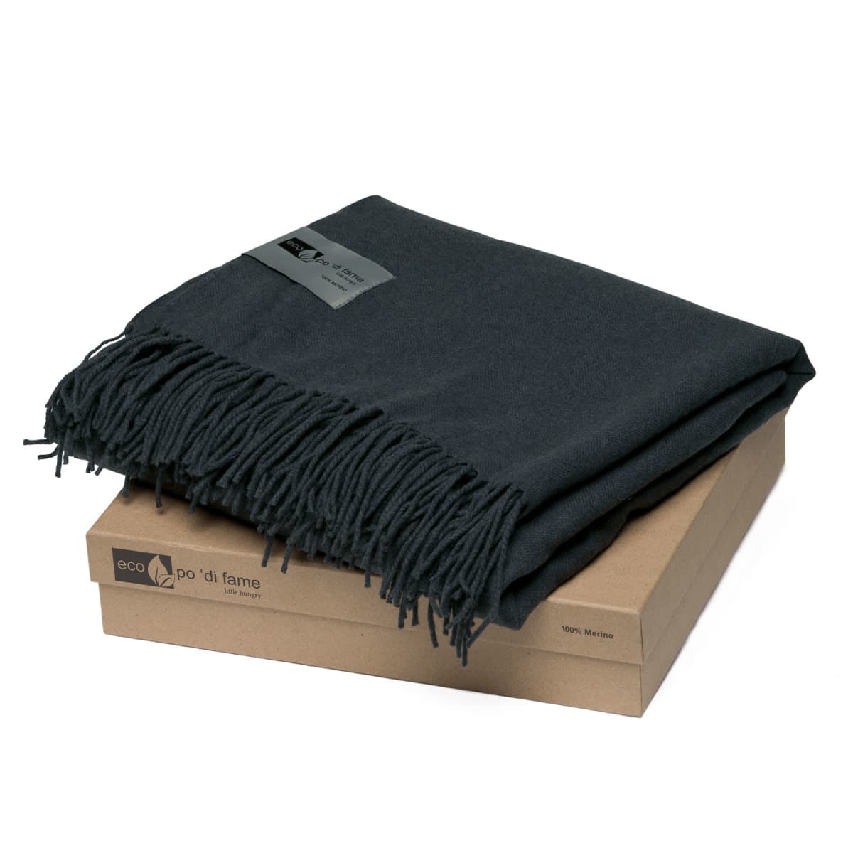 A folded dark gray wool blanket with fringe is placed on top of a brown eco-labeled cardboard box, showing a tag indicating its material and brand.
