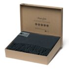 A charcoal gray fringed scarf neatly folded inside an open cardboard box. The box lid is propped open with text printed inside.