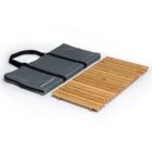 A foldable, wooden slat table laid next to a gray carrying case with black handles, designed for portability and outdoor use, on a white background.