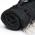 A rolled-up herringbone-patterned picnic blanket with a leather strap and fringe details.