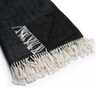 A folded black herringbone blanket with white tassels and a corner showing a water-resistant black fabric backing with water droplets.