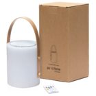 A cylindrical white speaker lamp with a leather handle next to its brown box packaging. A remote control with colorful buttons is placed in front. The box features an illustration and product name, po di fame, little hungry.