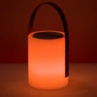 A cylindrical portable lamp emits a warm orange glow. It features a sturdy handle, suggesting ease of transport. The background is partially illuminated by the lamps soft light, enhancing the ambiance.