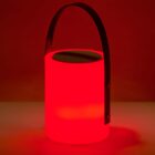 A glowing red cylindrical lantern with a black handle, set against a solid red background. The light emits a warm, soft glow, creating a cozy ambiance.