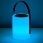 A portable cylindrical speaker with a handle is illuminated with a blue light, casting a soft glow against a dark background.