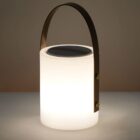 A portable, cylindrical LED lantern with a sleek metal handle. The lantern emits a soft, warm light and sits on a neutral background.