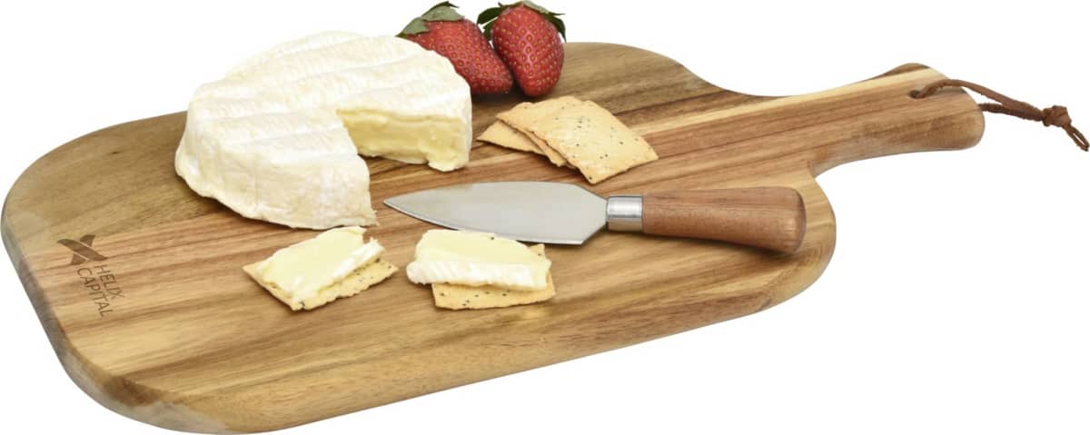 A wooden serving board with a knife, sliced brie cheese on crackers, and whole brie cheese. Two strawberries are also placed on the board.