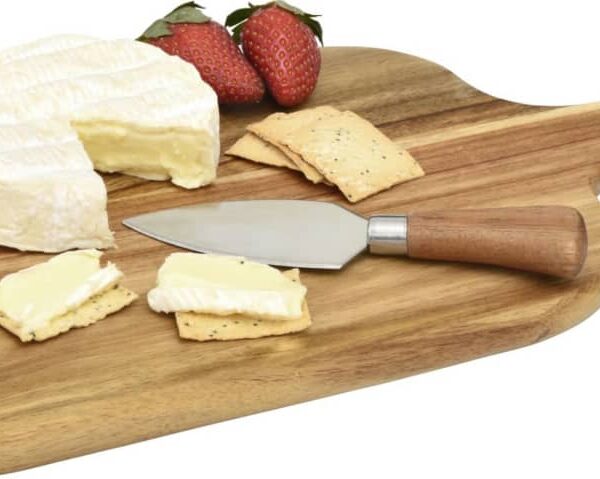 A wooden cutting board with a cheese wheel, partially sliced. Two strawberries and a few crackers with cheese are next to a small cheese knife on the board.