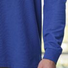 Person wearing a blue long-sleeve shirt and tan pants, arm slightly bent, indoors.