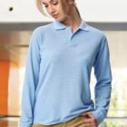 Woman in a light blue long-sleeve polo shirt and tan pants, looking down thoughtfully.