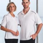 A woman and a man stand side by side, both wearing white polo shirts with black stripes on the shoulders. The background features frosted glass windows. The woman has short blonde hair and the man has short dark hair. Both are looking at the camera.