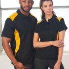 Two people in matching black and yellow collared shirts standing side by side indoors.