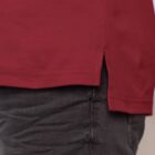 Close-up of the lower portion of a person wearing a red shirt and dark pants. The shirt has a small side slit at the hem, displaying the fabric texture.