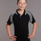 A young person with short dark hair smiles, wearing a black polo shirt with gray and white accents. Their hands rest on their hips. The background is plain and neutral.