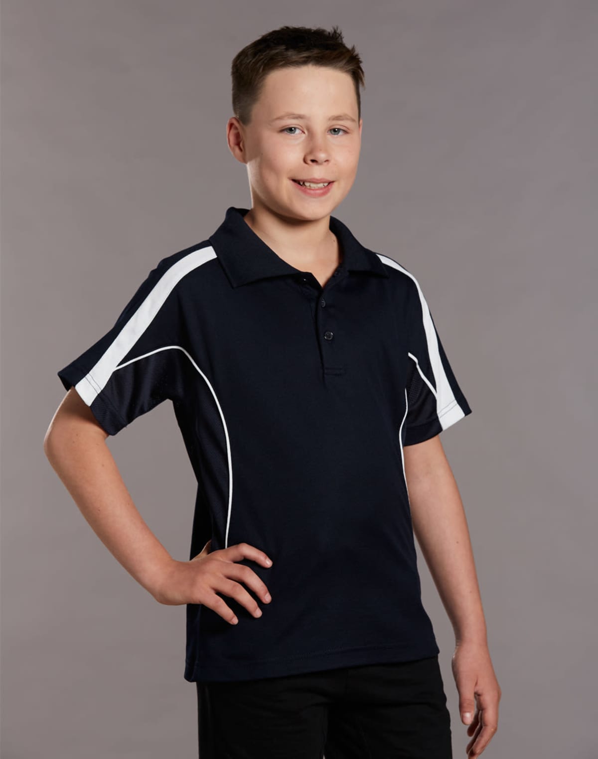 A young person wearing a black polo shirt with white stripes on the sleeves stands against a plain gray background, smiling and posing with one hand on their hip.