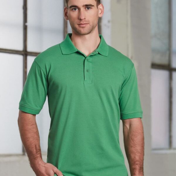 A person wearing a green polo shirt stands indoors against a backdrop of large windows. They have short brown hair and are looking directly at the camera.