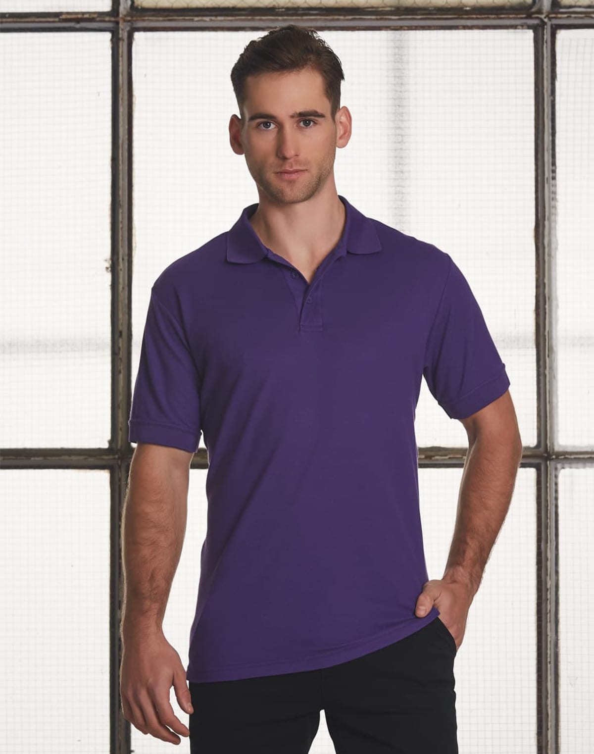 Person in a purple polo shirt standing in front of a windowed background.