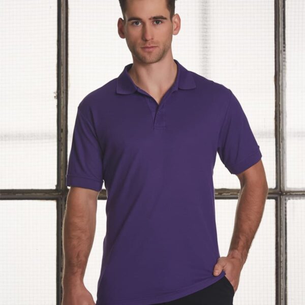 Man in a purple polo shirt stands against grid window.