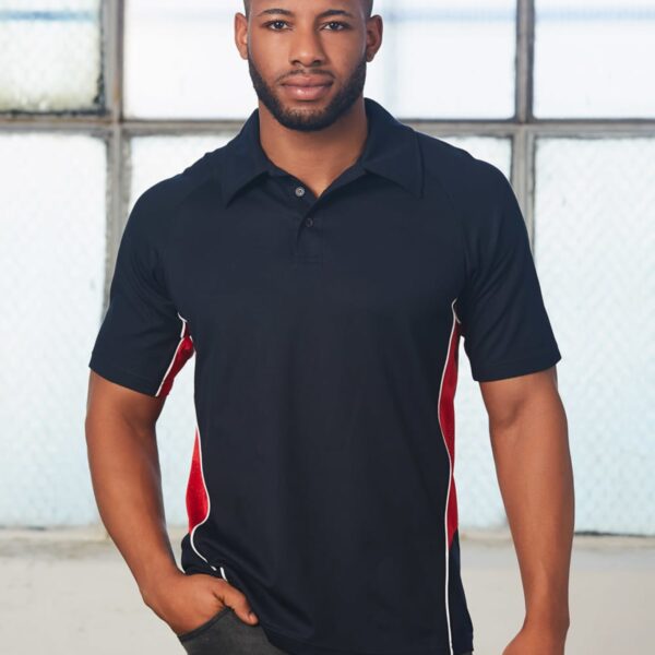 Man with a beard wearing a black polo shirt with red and white accents, standing in front of large windows.