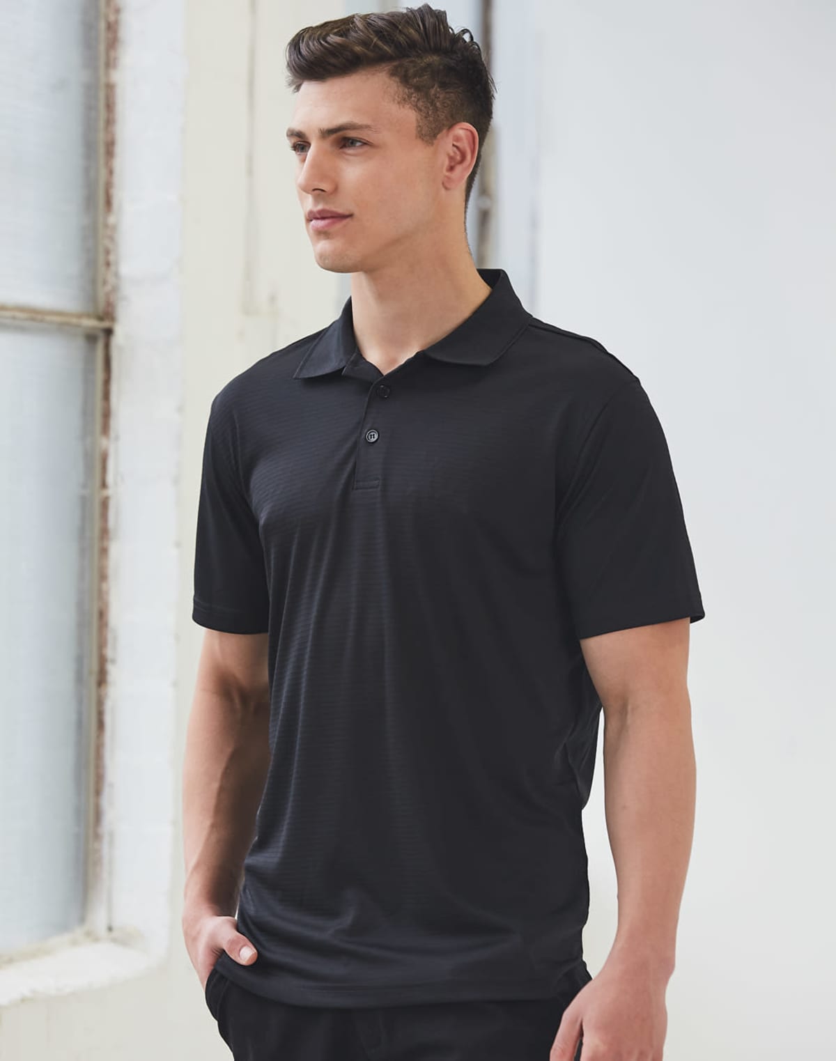 Man in black polo shirt standing near a window.