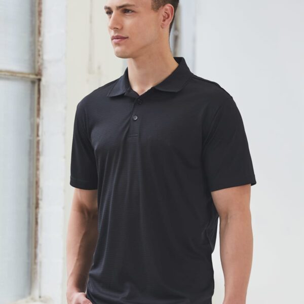 Man wearing a black polo shirt standing near a window.